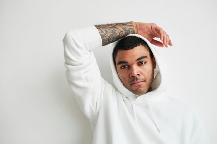 minimal-portrait-tattooed-young-man-wearing-white-hoodie-looking-camera-copy-space